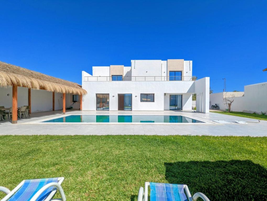 a house with a swimming pool and two lawn chairs at Villa AZMIR Djerba in Arkou