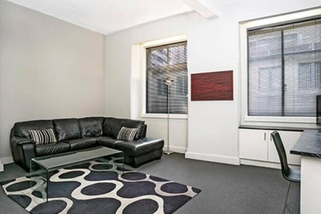 a living room with a black leather couch and a rug at CLD01 - 1 bedroom unit - Bridge Street, Sydney CBD in Sydney