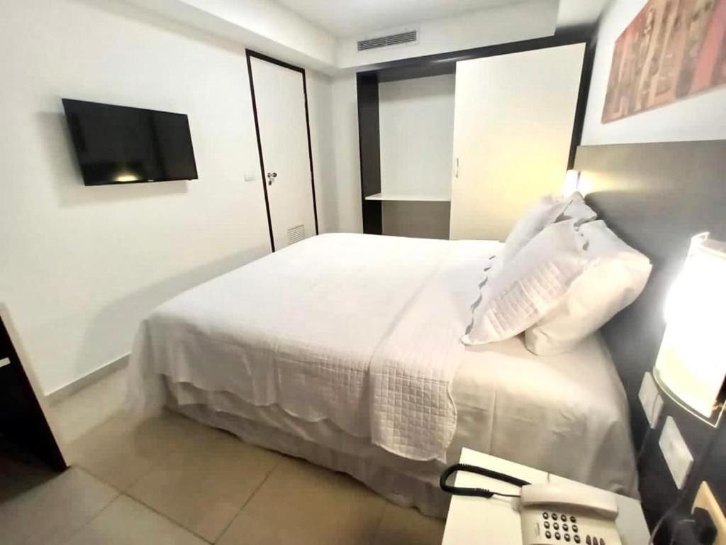 Habitación de hotel con cama blanca y teléfono en MARINAS PRAIA FLAT, en João Pessoa