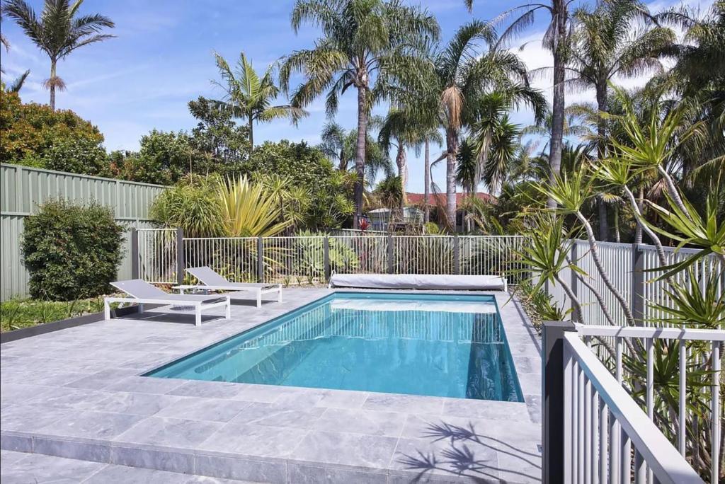 a swimming pool in a yard with a fence and palm trees at Kokomo on Village in Ulladulla