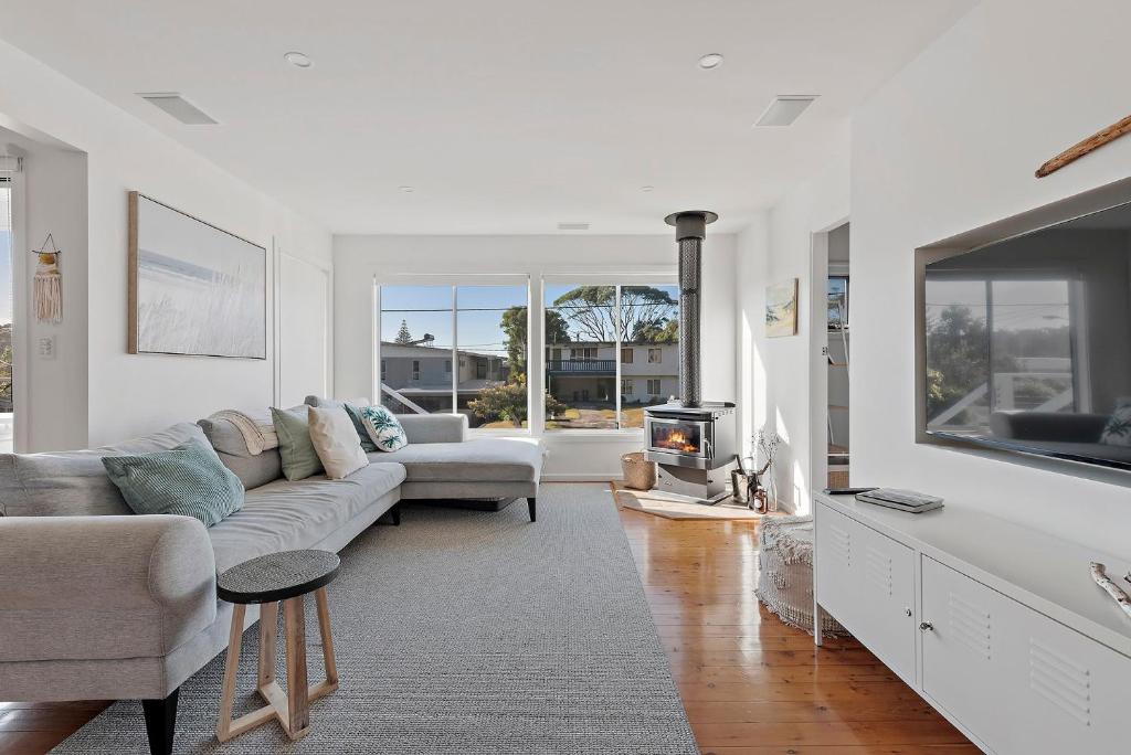 a white living room with a couch and a tv at Breezeway Mollymook in Mollymook