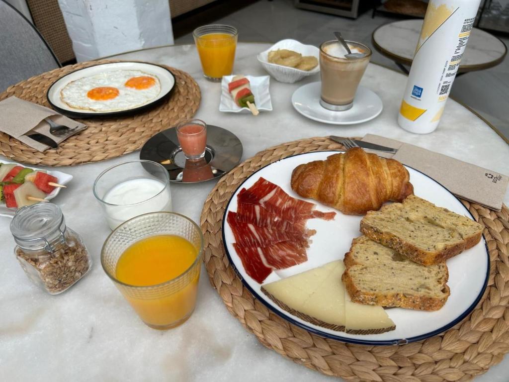 Mesa de caféda manhã do hotel One Shot Conde Torrejón com dois pratos com fatias de pão, ovos, salame, croissaint, copos de suco de laranja em uma mesa de mármore.