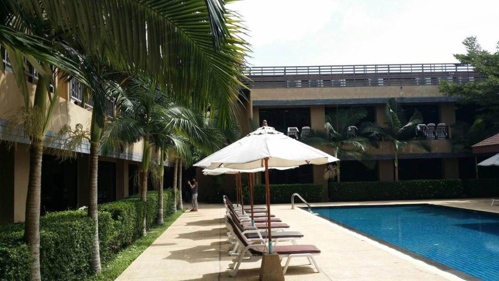 a pool with chairs and an umbrella next to a building at Naiyang Beach Hotel SHA Plus in Nai Yang Beach