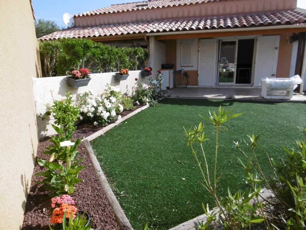 un jardin avec de l'herbe verte et des fleurs devant une maison dans l'établissement HOLIDAYLAND NARBONNE PLAGE Villas 6 ou 7 PERSONNES AVEC TERRASSE ET PLACE DE PARKING PRIVATIVE, à Narbonne