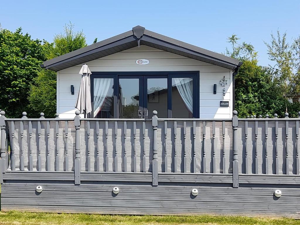 una pequeña casa con una valla y una sombrilla en Pebble Lodge en Tydd Saint Giles