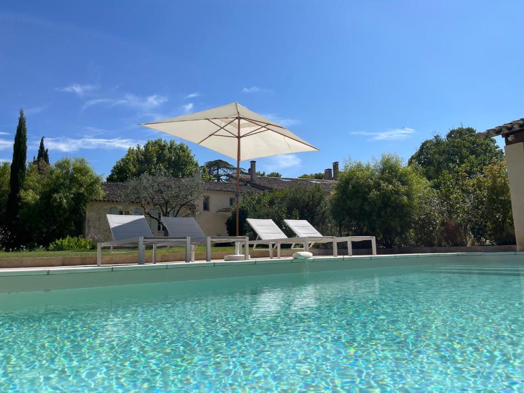 una piscina con 2 sillas y una sombrilla en Mas Millésime - Gîtes Carignan - 4 pers - piscine privative - St Remy de Provence, en Mas blanc des Alpilles