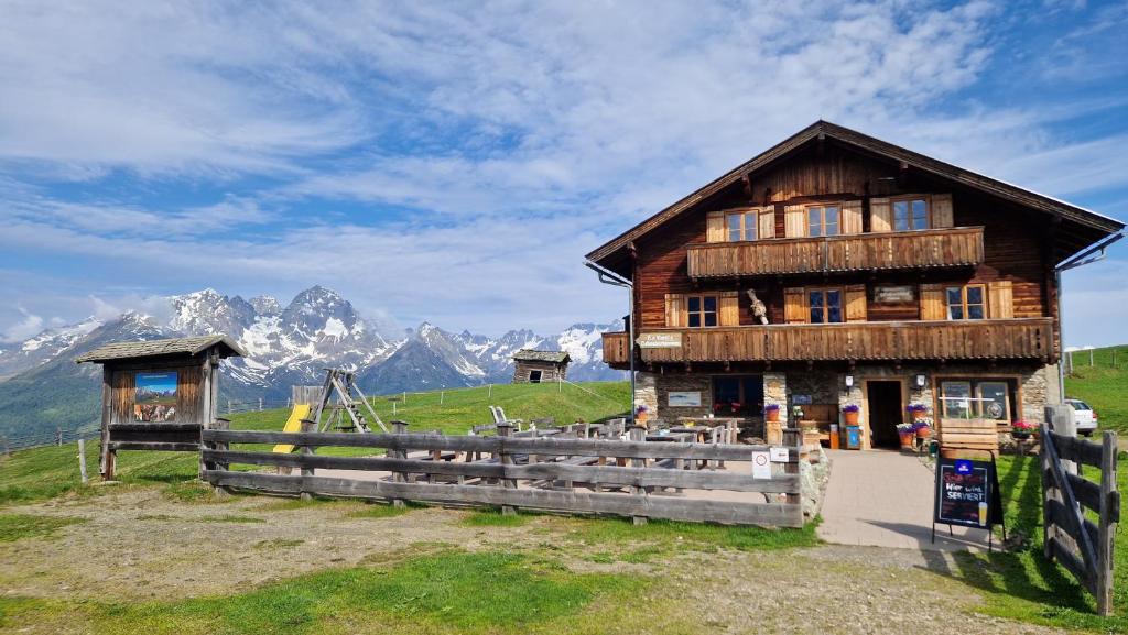 una casa in legno su una collina con montagne sullo sfondo di Almgasthaus Glocknerblick a Grosskirchheim