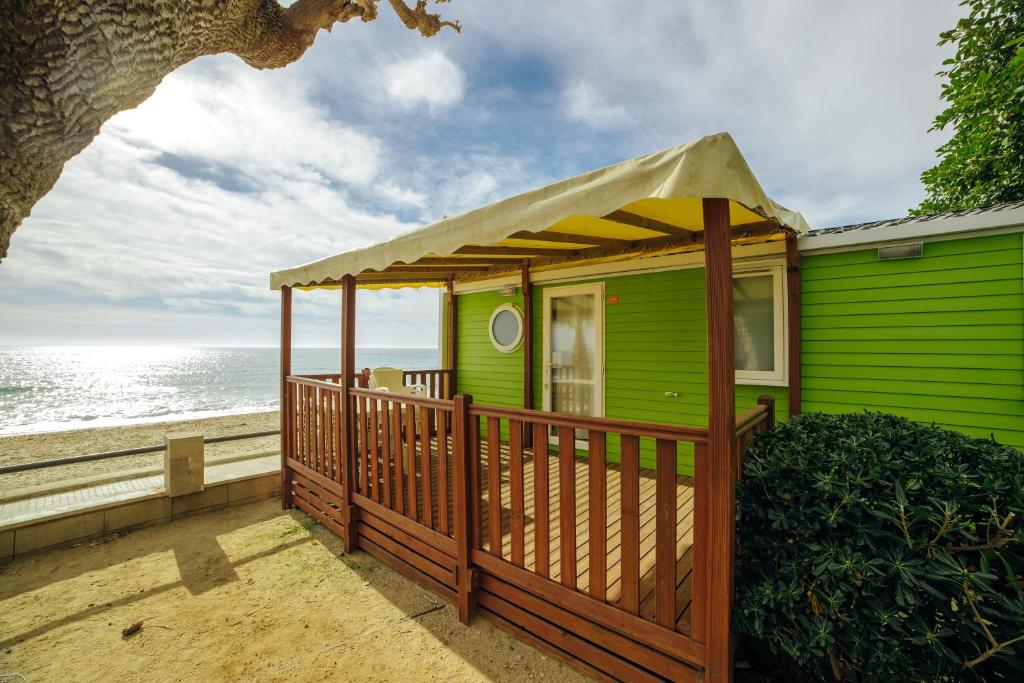 a green house with a wooden deck next to the ocean at Alannia Costa Dorada in Platja de l’Almadrava