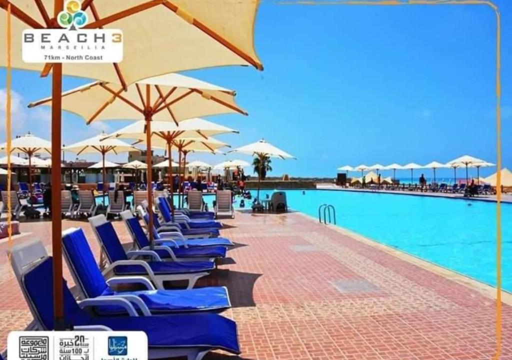 una fila de sillas de playa con sombrillas junto a una piscina en شاليه قرية مرسيليا بيتش 3 مارسيليا عائلات فقط - Marseilia Beach 3 chalet Families Only, en Dawwār Muḩammad Abū Shanab