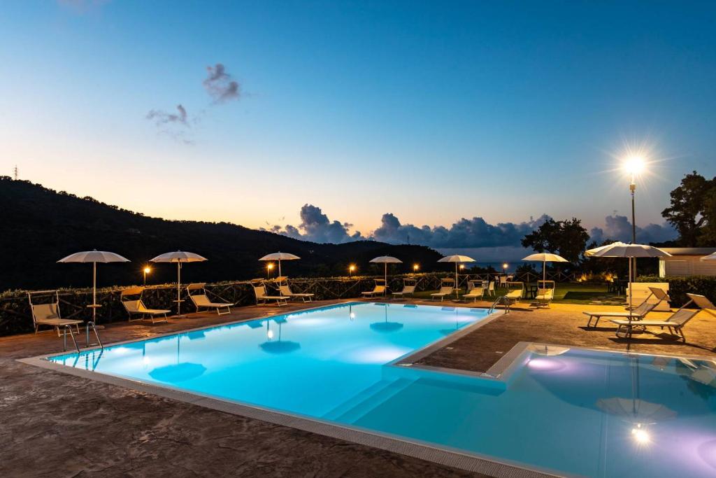 uma grande piscina com cadeiras e guarda-sóis à noite em Villa Ginevra Resort Agrituristico em Ficarra