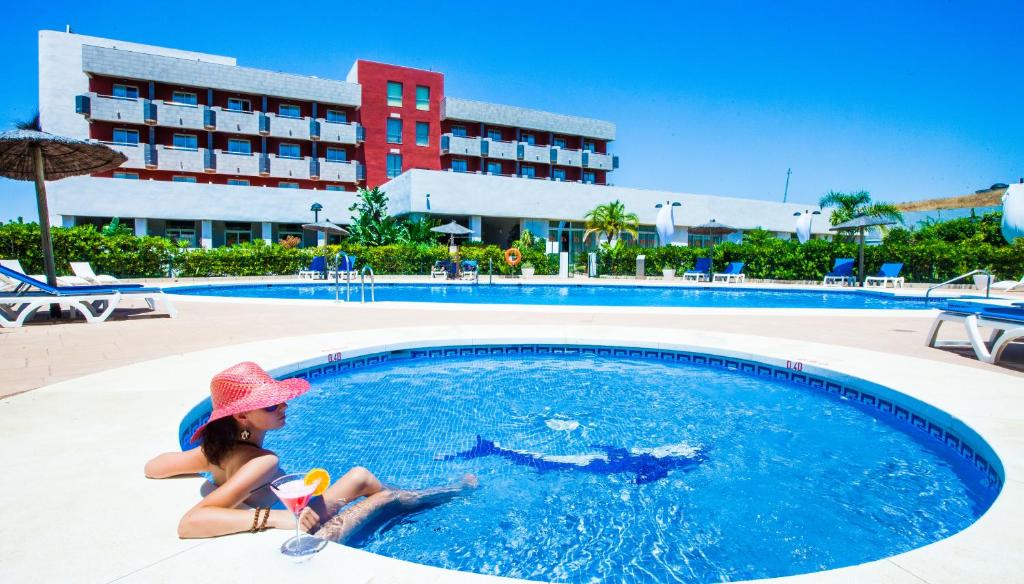una joven con sombrero sentada en una piscina en Hotel Montera Plaza, en Los Barrios
