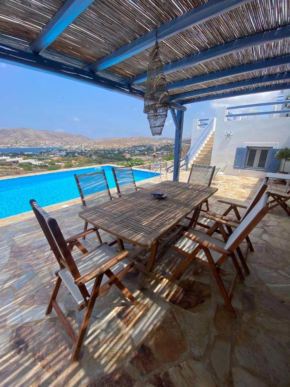 a wooden table and chairs on a patio with a pool at Syrona in Posidhonía