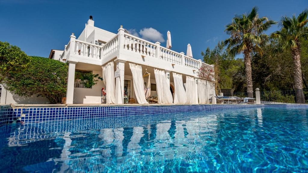 a white house with a swimming pool and palm trees at Can Paradís in San Antonio