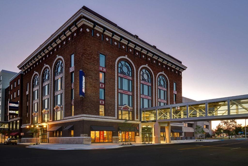 Hilton Garden Inn Kalamazoo Downtown في كالامازو: مبنى كبير من الطوب وامامه جسر