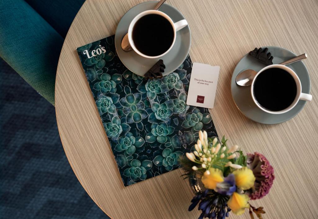 a table with two cups of coffee and a tray with flowers at Leonardo Royal Hotel Brighton Waterfront in Brighton & Hove