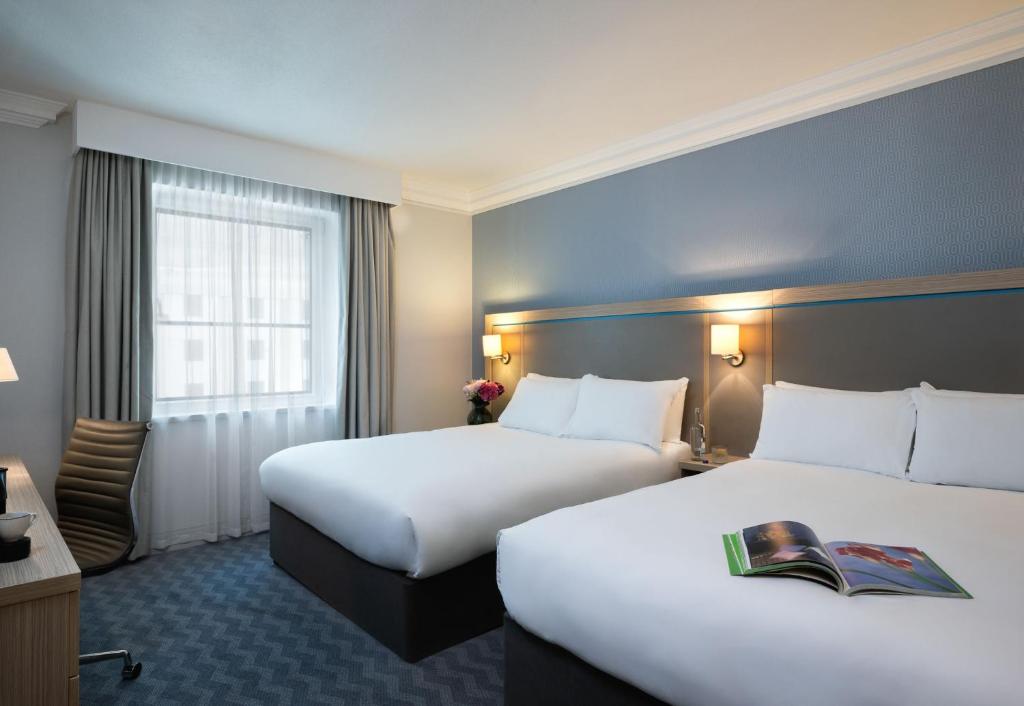 a hotel room with two beds and a desk at Leonardo Royal Hotel Brighton Waterfront in Brighton & Hove