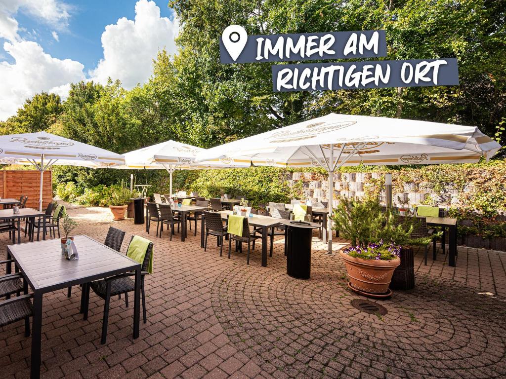 ein Restaurant im Freien mit Tischen und weißen Sonnenschirmen in der Unterkunft ACHAT Hotel Egelsbach Frankfurt in Egelsbach