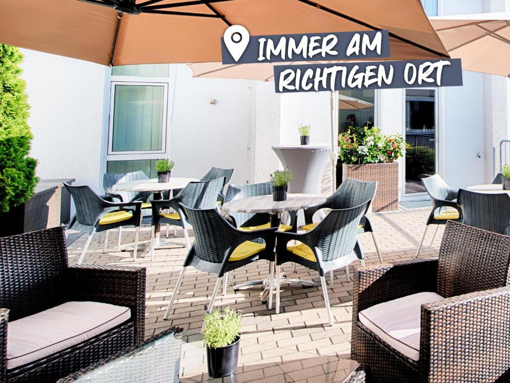 un patio extérieur avec des tables, des chaises et un parasol dans l'établissement ACHAT Hotel Hockenheim, à Hockenheim