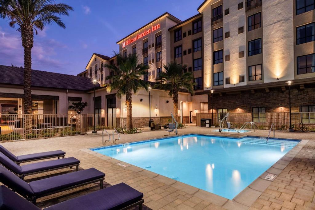 a hotel with a large swimming pool and palm trees at Hilton Garden Inn Pomona, CA in Pomona