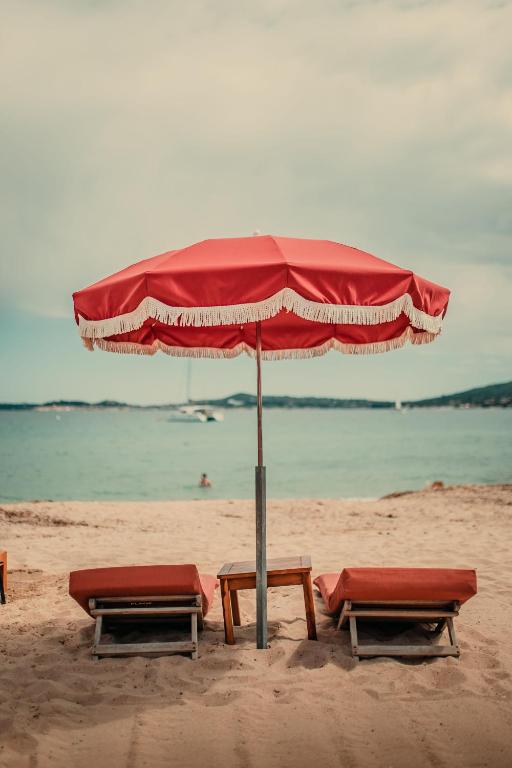 two benches and an umbrella on the beach at Les Prairies de la Mer in Grimaud