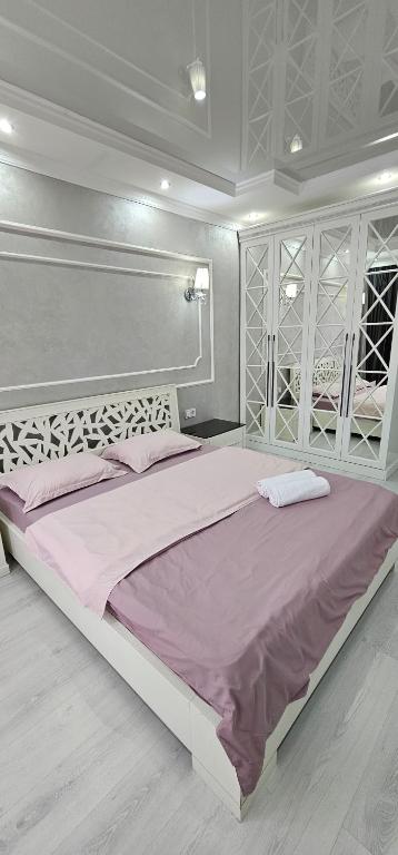 um quarto branco com uma cama grande e lençóis cor-de-rosa em Отличные апартаменты самом центре Алматы. Жилой комплекс Арбат em Almaty