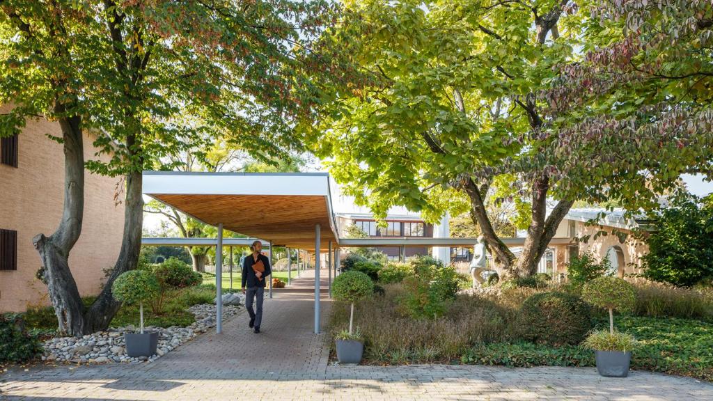 a person walking through a pavilion in a garden at Hotel Coop Tagungszentrum & Hotelpark im Grünen in Muttenz