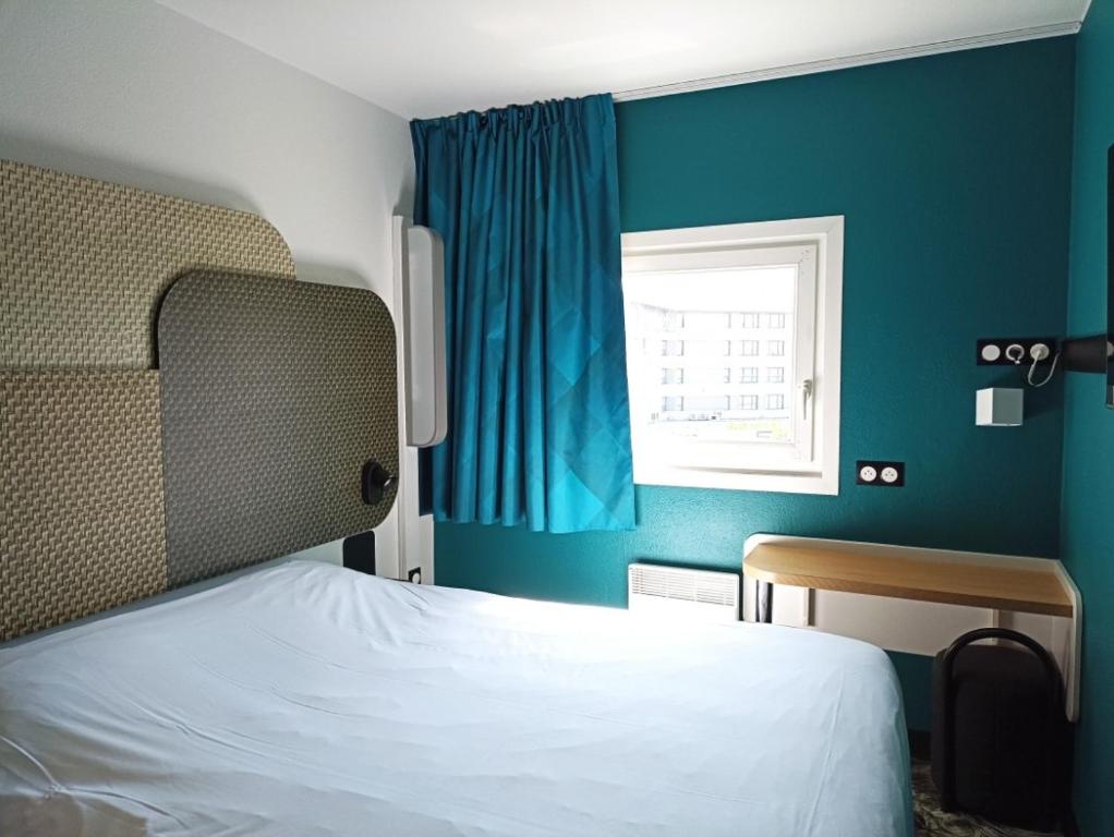 een slaapkamer met een bed met een blauwe muur en een raam bij B&B HOTEL Calais Terminal Cité Europe 2 étoiles in Coquelles