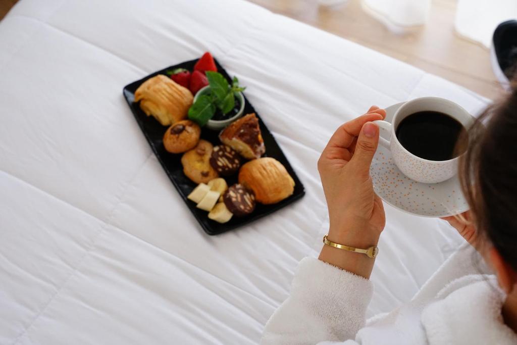 a woman holding a cup of coffee and a plate of food at Doanesia Premium Hotel & Spa in Tirana