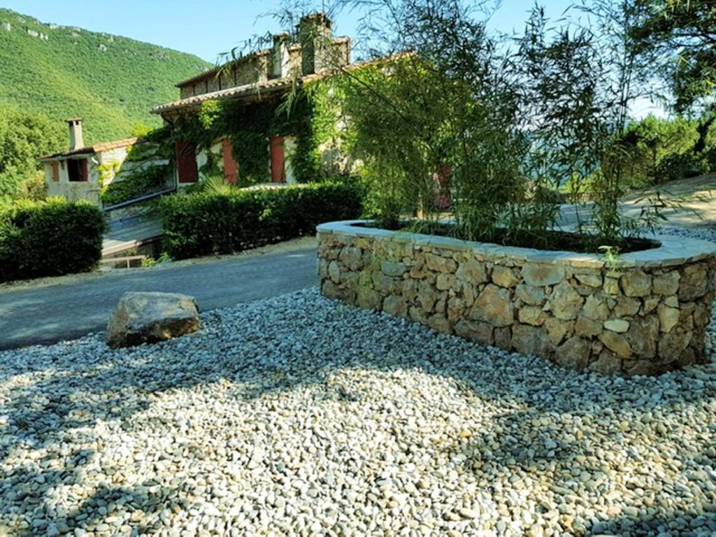 a house with a stone wall next to a road at Maison confortable avec piscine à Saint-Julien-de-la-Nef in Saint-Julien-de-la-Nef