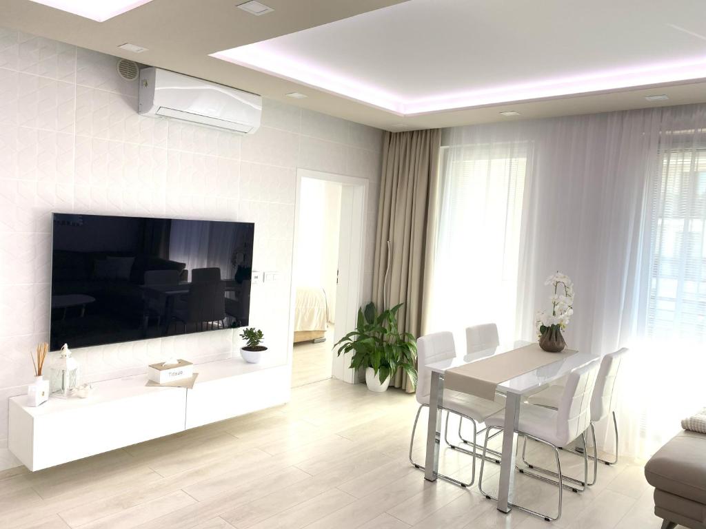 a white living room with a table and a large tv at Die Eleganz - Exclusive Apartment near the City Center with Free Private Parking in Bratislava