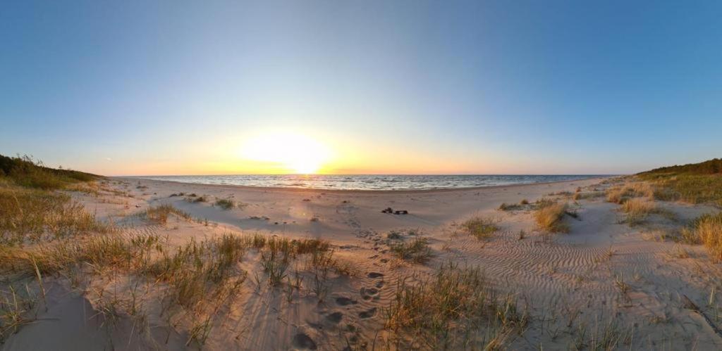 um pôr do sol numa praia com pegadas na areia em Seaside holiday home Vecvalki em Saunags