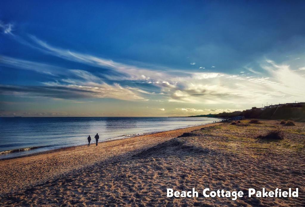two people walking on a beach with the ocean at Beach Cottage Pakefield- Newly Fully Renovated House in Pakefield