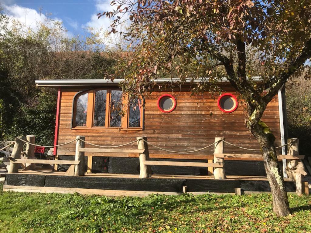 una cabaña de madera con un banco y un árbol en Les roulottes de Moulin Rouge, en Audelange