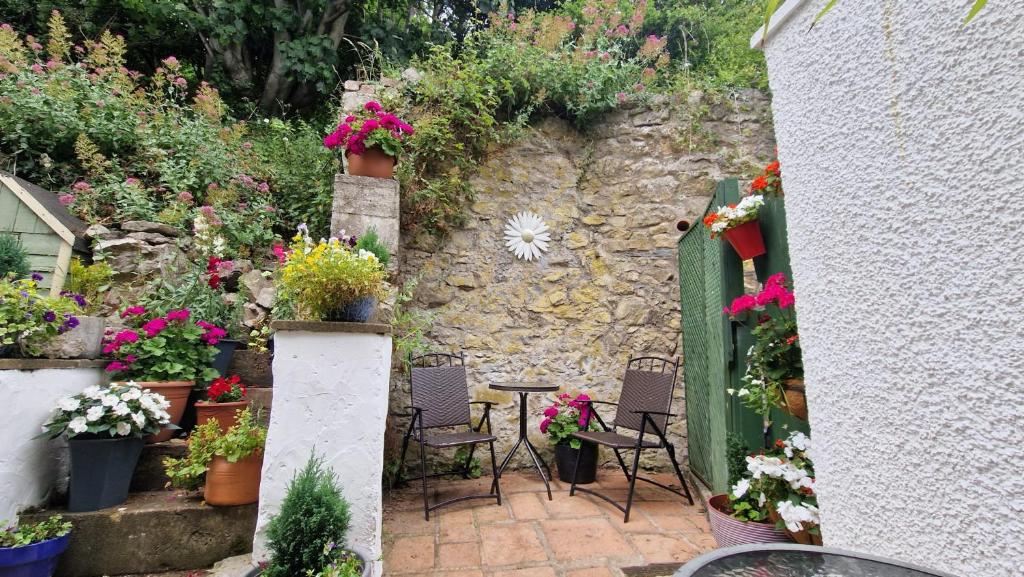 einen Garten mit Stühlen, Blumen und einer Steinmauer in der Unterkunft Copper Mine Cottage in Llandudno