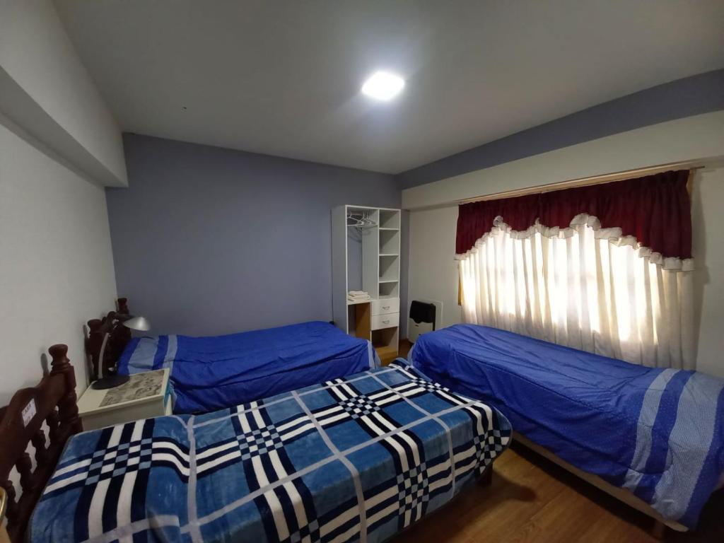1 dormitorio con 2 camas con sábanas azules y ventana en hostel comunidad Ushuaia en Ushuaia
