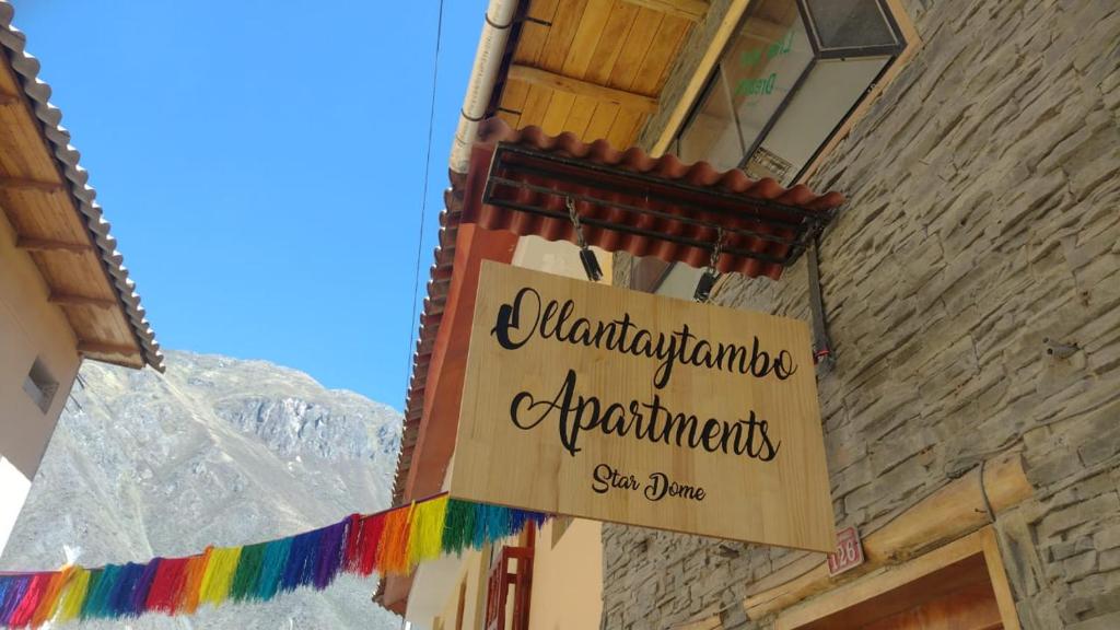 un panneau sur le côté d'un bâtiment avec une bannière arc-en-ciel dans l'établissement hostal ollantaytambo apartments, à Ollantaytambo