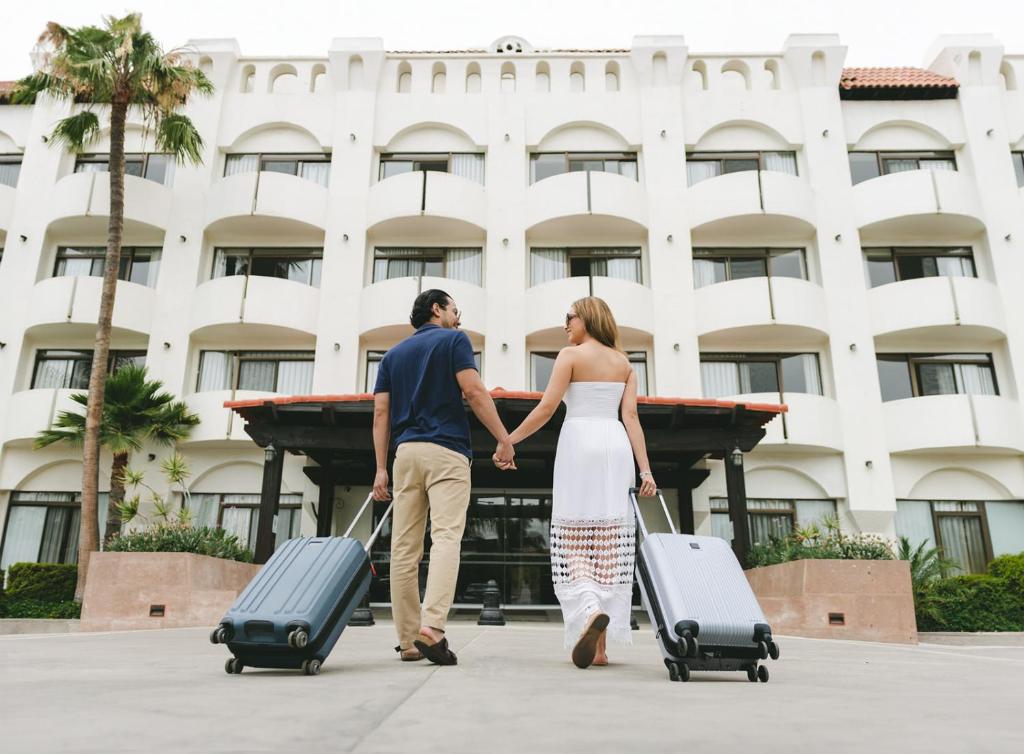 un hombre y una mujer caminando con su equipaje en Corona Hotel & Spa en Ensenada