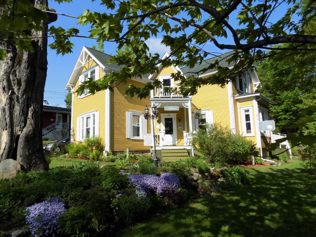 una casa amarilla con flores en el patio en À L'Ancestrale B&B, en Magog-Orford