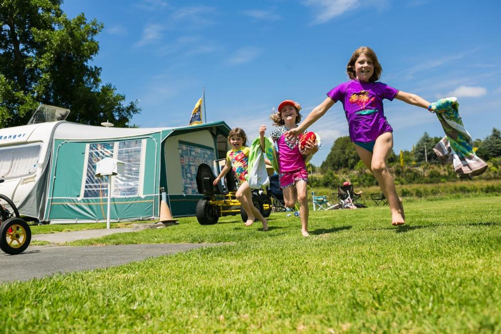 un grupo de niños corriendo en la hierba cerca de una caravana en Whanganui River Top 10 Holiday Park, en Whanganui