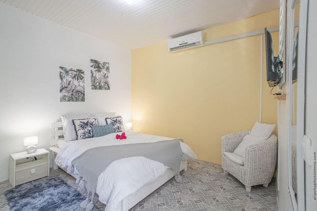 een slaapkamer met een wit bed en een stoel bij Apt La Source - Plage à 5min - Nature & Calme in Les Trois-Îlets