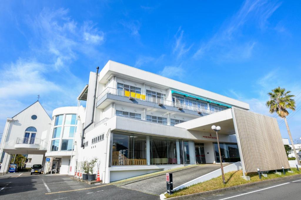 a white building with a palm tree in front of it at Amakusa Santacoming Hotel in Amakusa