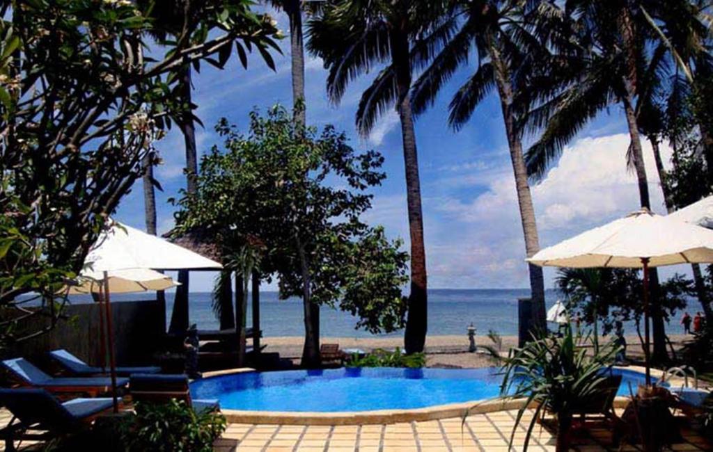 einen Pool mit Sonnenschirmen und Stühlen sowie das Meer in der Unterkunft Bali Bhuana Beach Cottages in Amed
