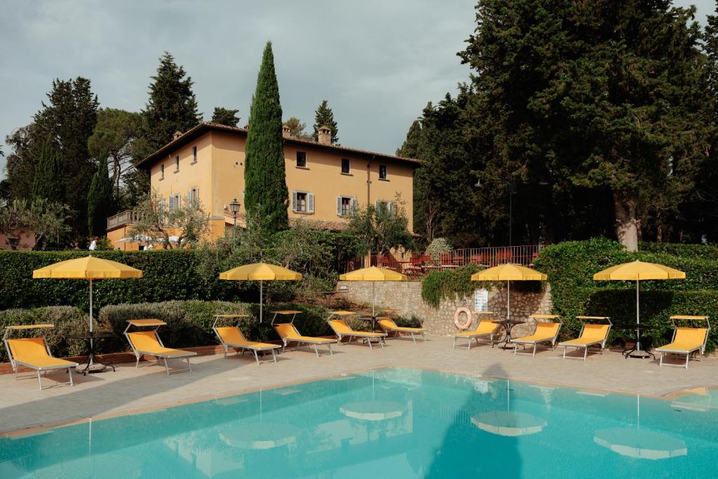uma piscina com cadeiras e guarda-sóis em frente a um edifício em Villa La Cappella em Montespertoli