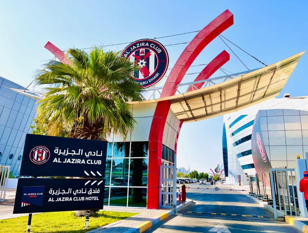 a palm tree in front of a building with a sign at Al Jazira Club Hotel in Abu Dhabi