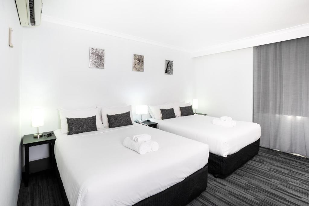 Joondalup City Hotel في بيرث: سريرين في غرفة الفندق بجدران بيضاء