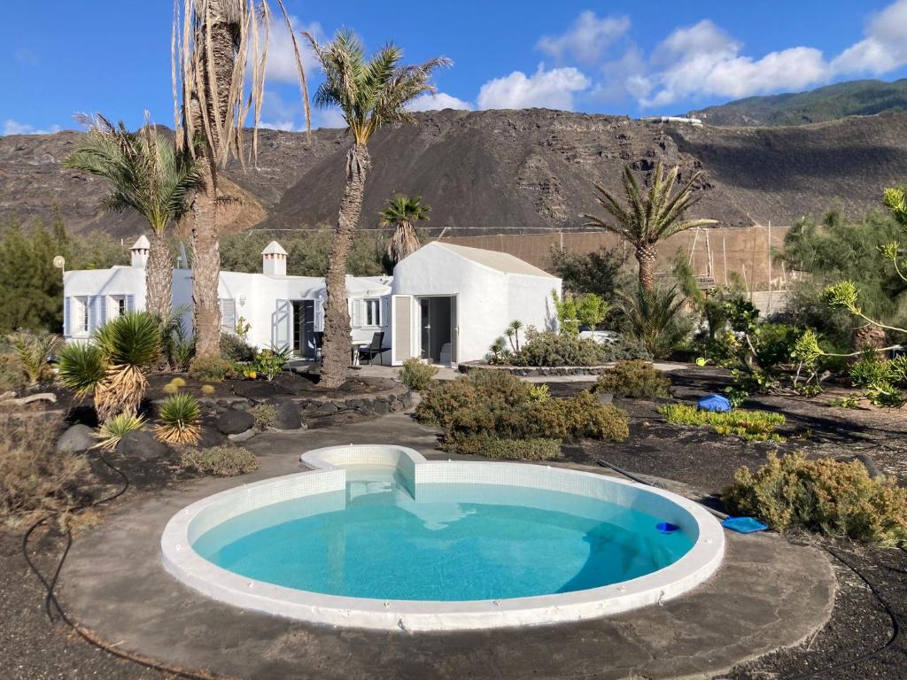 een zwembad in een tuin met een huis en palmbomen bij Strandhaus in Los Llanos de Aridane