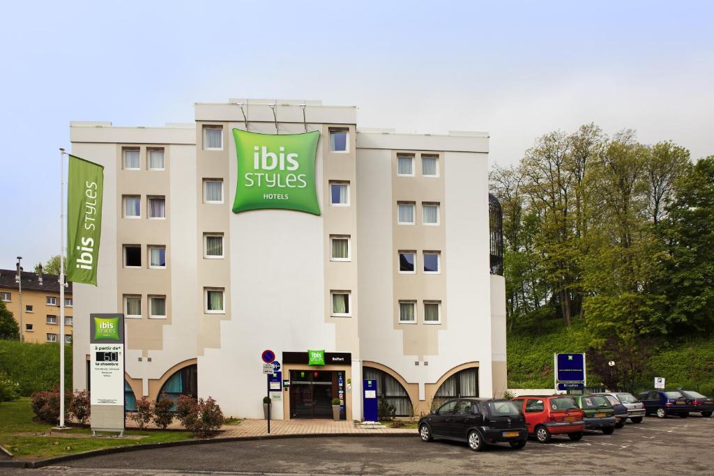un hôtel avec des voitures garées sur un parking dans l'établissement ibis Styles Belfort Centre, à Belfort