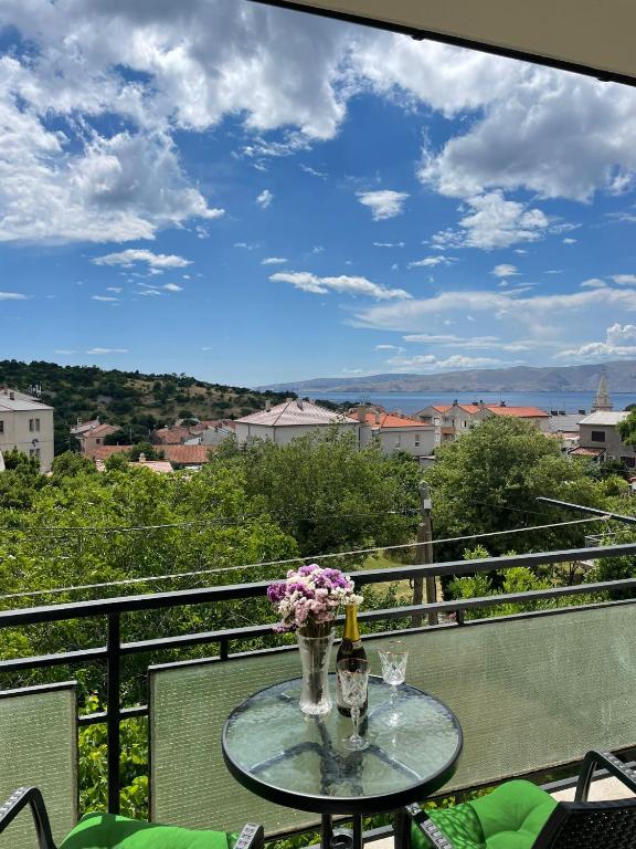 a glass table with a bottle of wine and flowers on a balcony at Apartment " So" in Senj
