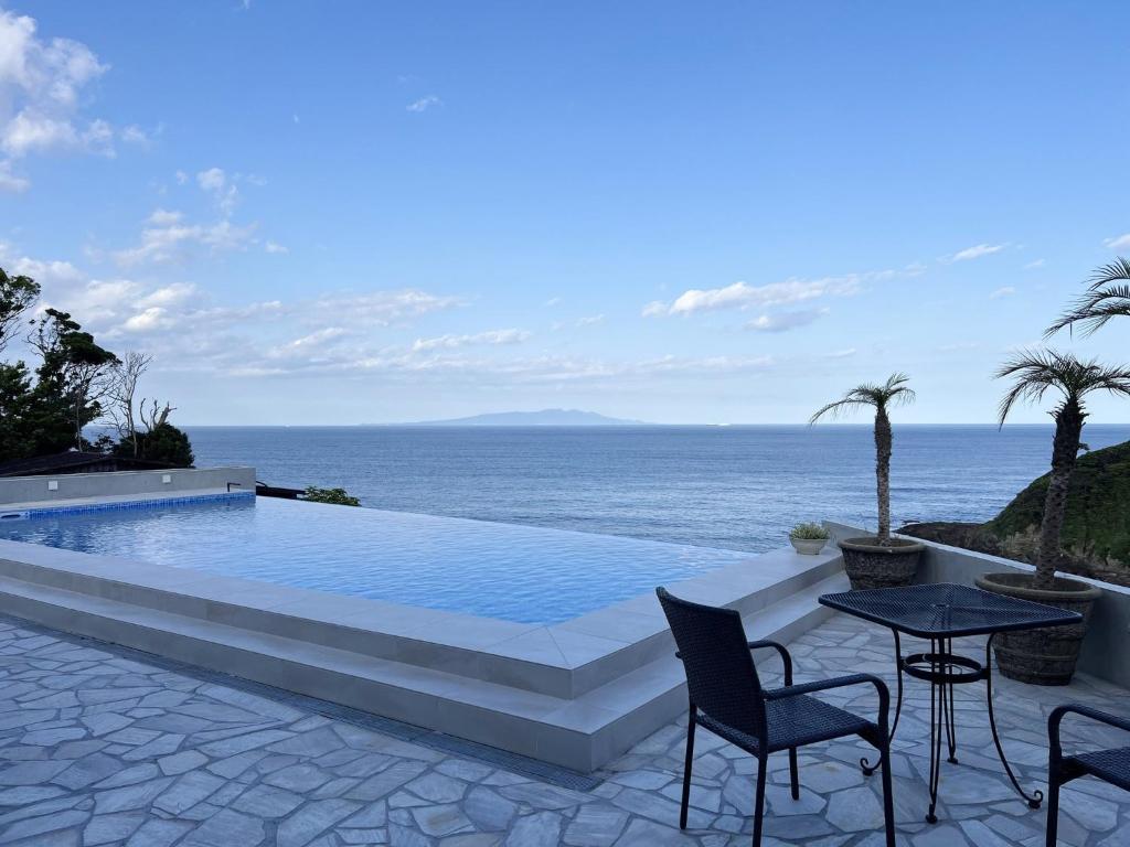 una piscina con mesa y sillas y el océano en Gardenvilla Shirahama, en Shimoda