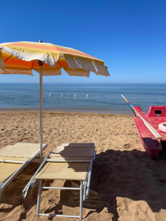 a beach with an umbrella and a chair and a boat at Hotel Miramare Garzia in Marinella di Selinunte